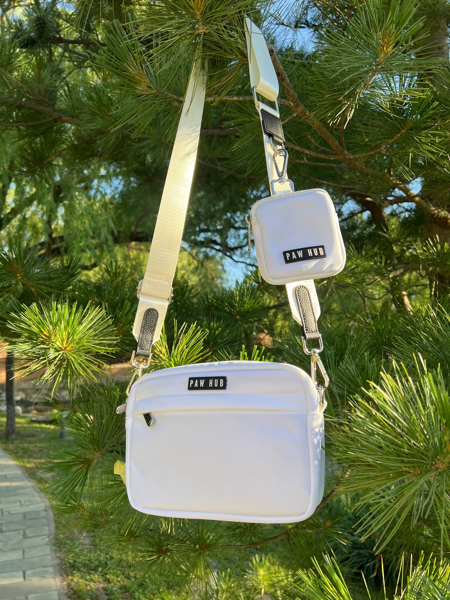 White dog bag with strap against a green tree background